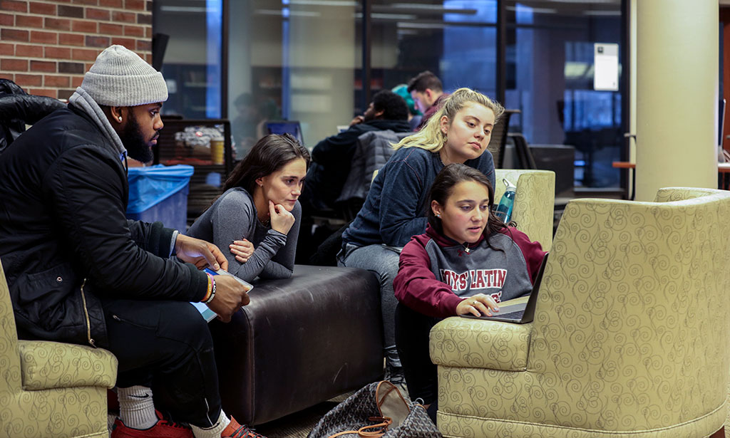 Students gather around a laptop in the library